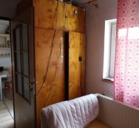 Ein Zimmer in einer Zweizimmerwohnung mit offenen Türen, einem Schrank und einem Vorhang mit rotem Muster.