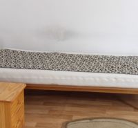 Ein Bett in einem Zimmer mit einem Holzboden, daneben ein Holzschrank.