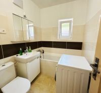 Badezimmer im Einfamilienhaus mit Badewanne, Waschmaschine und Waschbecken, helle Fliesen.