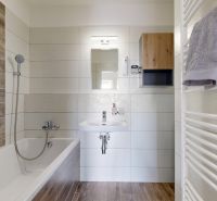 Badezimmer mit Badewanne, Boden in Holzoptik und weißen Fliesen in einer 3-Zimmer-Wohnung.