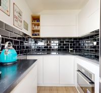 Kompakte Küche in einer 3-Zimmer-Wohnung mit schwarzen glänzenden Fliesen und einem Boden in Holzoptik.