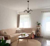Wohnzimmer mit Holzboden, beigem Sofa und rundem Teppich.