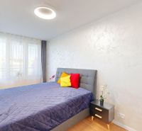 Helles Schlafzimmer mit Bett, Nachttisch und bunten Kissen in einer 2-Zimmer-Wohnung.