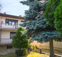 Ein Einfamilienhaus in Jelenec mit Balkon, umgeben von Grün und Nadelbäumen.