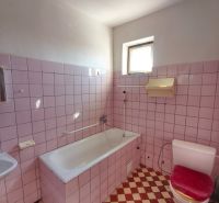 Ein Badezimmer mit rosa Fliesen und einer weißen Badewanne in einem Einfamilienhaus.