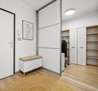 Eingangsbereich mit weißem Schrank, Bank, Dekoration und Boden mit Holzdekor in einer 2-Zimmer-Wohnung.