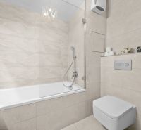 Badezimmer mit Badewanne und Toilette in einer 2-Zimmer-Wohnung mit heller Fliesenverkleidung.