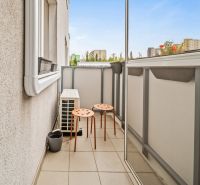 Balkon mit zwei orangefarbenen Stühlen in einer Zweizimmerwohnung mit Blick auf die Stadt.