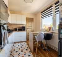 Küche in einer 3-Zimmer-Wohnung mit Holzdekor, weißen Möbeln und dekorativem Teppich.
