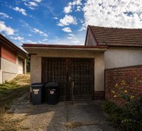 Einfamilienhaus mit Garage in Šalgočka, mit zwei Mülleimern und einer Ziegelmauer.
