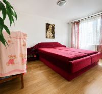 Schlafzimmer im Einfamilienhaus mit rotem Bett und Boden in Holzoptik.