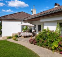 Ein Einfamilienhaus in Šalgočka mit Terrasse, Garten und Sonnenschirm auf einem Rasenstück.