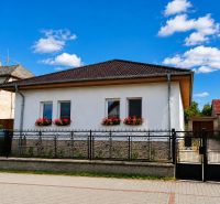 Ein Einfamilienhaus in Šalgočka mit weißer Fassade, Fensterblumen und einem Walmdach.