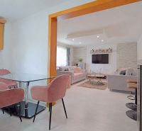 Innenraum eines Einfamilienhauses mit rosa Stühlen, Glastisch und Wohnzimmer mit Sofa.