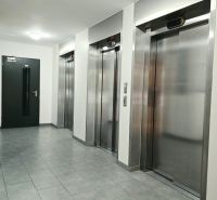 Ein Flur mit vier Metallaufzügen und grauen Fliesen in einer Vierzimmerwohnung.