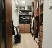 Ein Kleiderschrank mit Schränken und Regalen in einer 4-Zimmer-Wohnung mit einem Boden in Holzoptik.