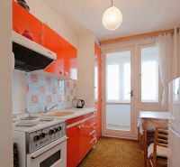 Küche in einer 2-Zimmer-Wohnung mit orangefarbenen Schränken und Balkontüren.