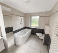 Ein Badezimmer in einem Einfamilienhaus mit weißer Sanitärausstattung und Badewanne, hellen Fliesen und einem Heizkörper.