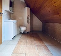 Ein Badezimmer in einem Einfamilienhaus mit schräger Holzdecke und hellen Fliesen.