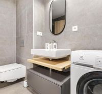 Badezimmer in einer Einzimmerwohnung mit moderner Waschmaschine und grauen Fliesen.