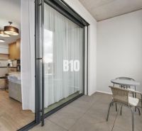 Ein Balkon mit Sitzgelegenheit und Blick in eine Einzimmerwohnung durch Schiebetüren.