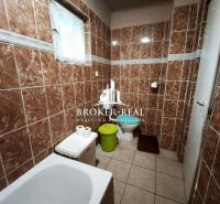 Ein Badezimmer mit braunen Fliesen, einer Badewanne, einer Toilette und einem Mülleimer in einem Einfamilienhaus.