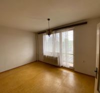 Ein leerer Raum in einem Einfamilienhaus mit einem Fenster, Vorhängen und einem Boden in Holzoptik.