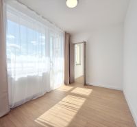 Ein helles Zimmer mit Vorhängen und einem Boden in Holzoptik in einer 3-Zimmer-Wohnung.