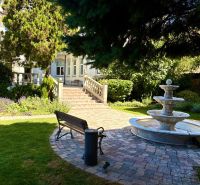 Ein Garten mit einem Brunnen, einer Bank und Grünflächen vor dem Gebäude.