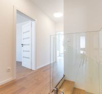Innenraum eines Einfamilienhauses mit Holzboden und Glasgeländer an der Treppe.