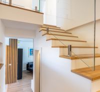 Innenraum eines Einfamilienhauses mit Holztreppe, Glasgeländer und Boden mit Holzdekor.