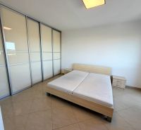 Helles Schlafzimmer mit Schiebetürenschrank, Bett und Fliesenboden in einer Einzimmerwohnung.