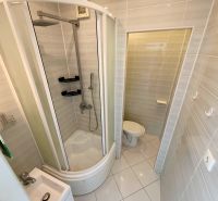 Badezimmer mit Duschkabine und Toilette in einer Einzimmerwohnung, helle Fliesen.