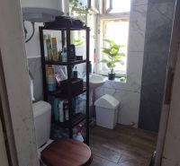 Badezimmer in einer 2-Zimmer-Wohnung mit Fenster, Regalen und Boden in Holzoptik.