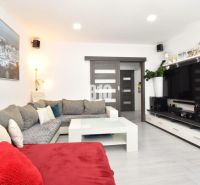 Wohnzimmer in einer 3-Zimmer-Wohnung mit Ecksofa, Fernseher und Boden in Holzoptik.