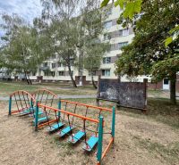 Fassade eines Wohnblocks in Topoľčany mit einem Kinderspielplatz und Vegetation rund um eine Einzimmerwohnung.