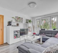 Wohnzimmer in einer 2-Zimmer-Wohnung mit einer Eckcouch und einem Boden in Holzoptik.