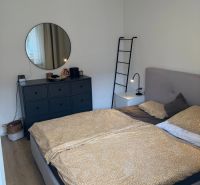 Schlafzimmer mit Bett, Kommode und rundem Spiegel in einer 3-Zimmer-Wohnung.