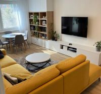 Wohnzimmer in einer 3-Zimmer-Wohnung mit einem bequemen Sofa, einem Esstisch und einem Boden in Holzoptik.