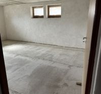 Ein unmöbliertes Zimmer in einem Einfamilienhaus mit zwei kleinen Fenstern und einem rohen Boden.