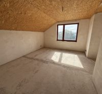 Innenraum eines Einfamilienhauses mit Fenster, schräger Decke und unbehandeltem Boden.