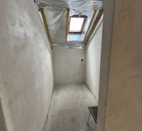 Ein schmaler Raum mit Betonboden und Dachfenster in einem Einfamilienhaus.