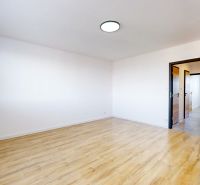 Ein Zimmer mit Holzboden in einer 3-Zimmer-Wohnung, weiße Wände, offene Türen.