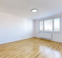 Ein geräumiges Zimmer mit großen Fenstern und einem Boden in Holzoptik in einer 3-Zimmer-Wohnung.