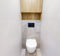 Eine Toilette mit Wänden aus weißen Fliesen in einer 3-Zimmer-Wohnung, mit einem Schrank über der Toilette.