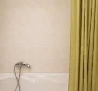 Badezimmer mit Badewanne, Duschvorhang und hellen Fliesen in einer 2-Zimmer-Wohnung.