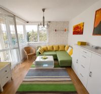 Wohnzimmer mit Ecksofa, Holzboden und buntem Teppich.