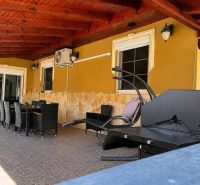 Die Terrasse des Einfamilienhauses in Darnózseli mit Rattanmöbeln und einem Grill unter einer Holzdecke.