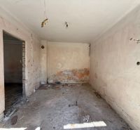 Ein Zimmer in einem Einfamilienhaus vor der Renovierung mit freiliegenden Wänden und Boden.