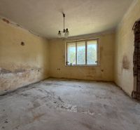 Ein Zimmer in einem Einfamilienhaus mit einem Fenster, abgebröckeltem Putz und unfertigem Boden.